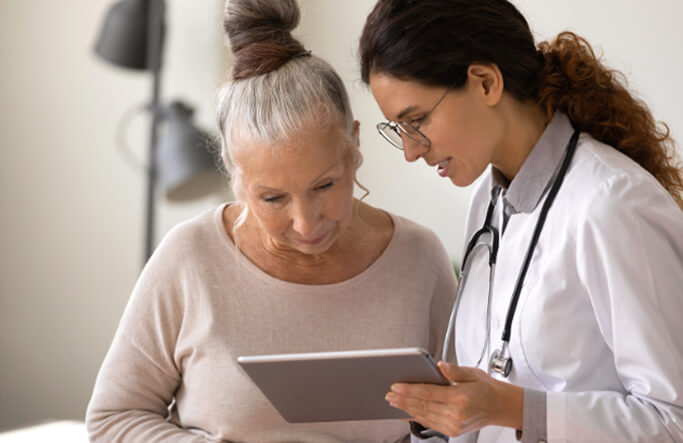 A female doctor speaking to a senior white woman while showing results on a tablet