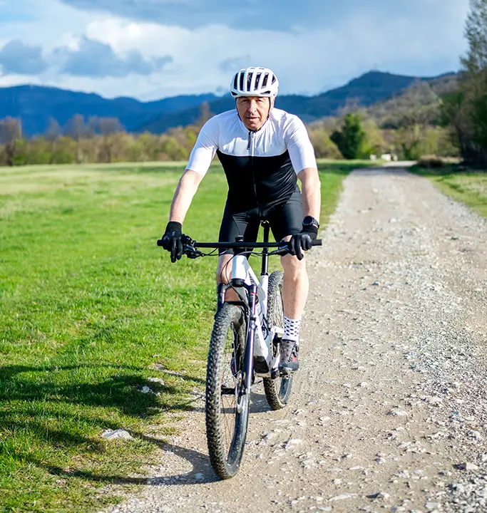 A senior, white male biking on a trail, with mountains in the background.