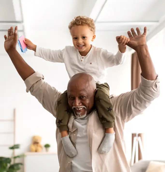 A grandparent holding his grandson on his shoulders.